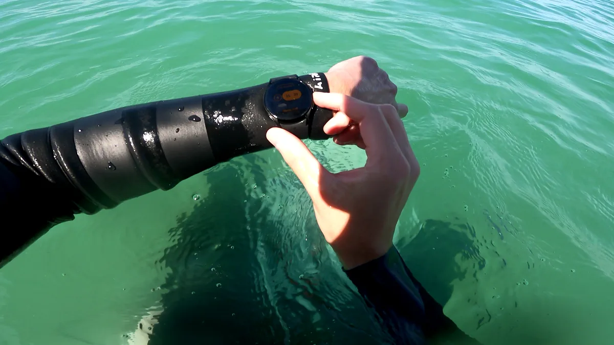 Un message du coach arrivant sur la montre connectée du surfeur Surfeur consultant une notification de message sur sa montre connectée dans l'eau